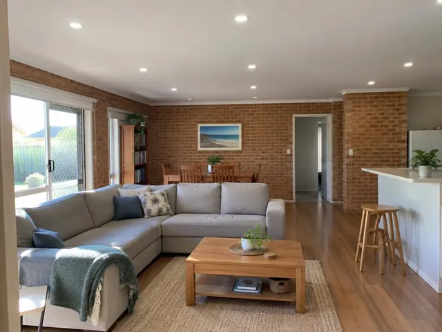 Living room with recessed downlights in a brick home interior with timber floors and open-plan dining in Budgewoi