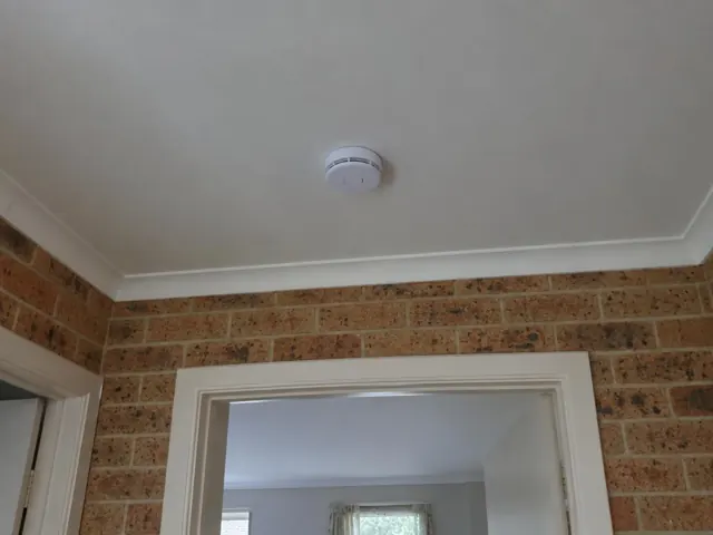 Ceiling-mounted smoke alarm above a brick wall doorway in a home in Noraville